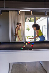 Naklejka premium Diverse female friends playing pool in modern game room wearing yellow sundress and lime top, cue
