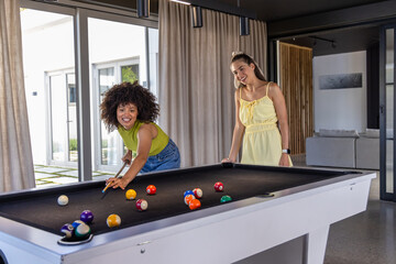Naklejka premium Diverse female friends playing pool at home lounge on white table with cue, balls, lime top