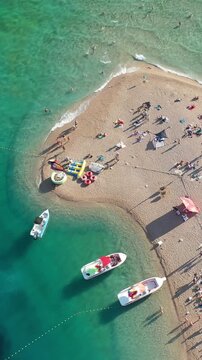 Vertical drone footage of the iconic Zlatni Rat beach in Bol, Croatia, showing boats, sunbathers and the vibrant summer atmosphere along the Adriatic coast