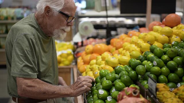 Senior man picks fresh fruits and vegetables while shopping in grocery store. He enjoys selecting ripe items for his meals.