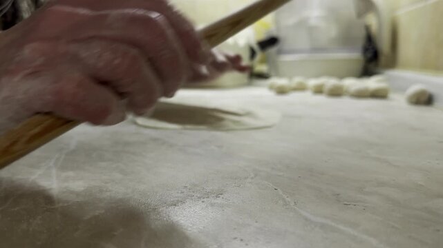Cook rolling out flatbread dough with thin wooden pin from low angle view
