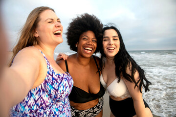 Three women smiling at the beach, enjoying a sunny day together.
