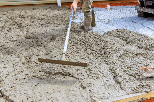 Worker is applying concrete on gravel using tool to create flat surface at construction location.
