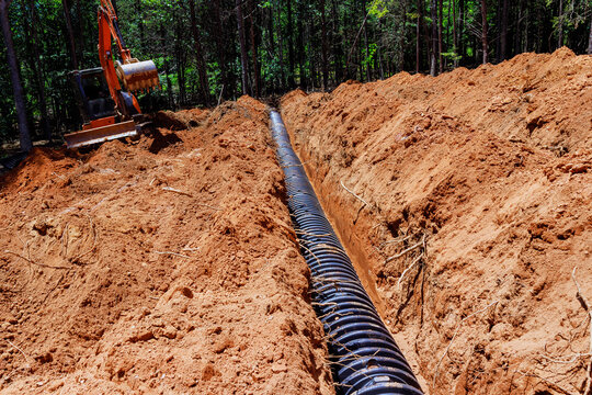 Heavy excavator is actively digging trench in ground for drainage septic chamber installation in forested location
