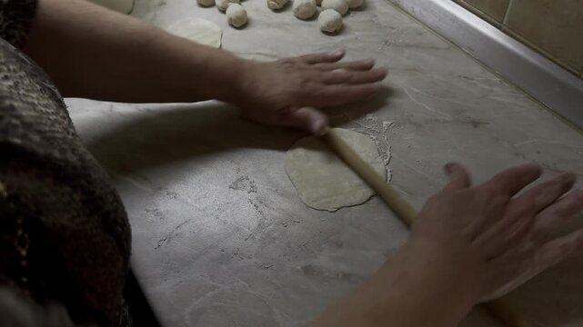 Cook rolling out small circles of dough with a thin wooden pin on counter