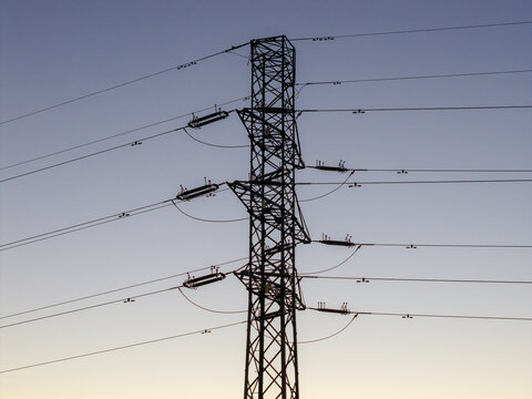 Aerial view of a high-voltage electricity pylon with power lines against a clear twilight sky in Warsaw, Masovian Voivodeship, Poland.