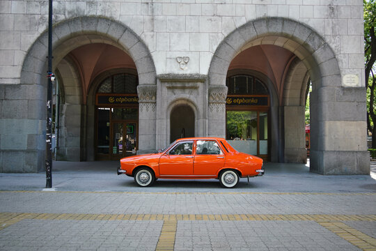 Side view of a historic orange Dacia 1300 oldtimer car parked under the stone arches of the historic Art Nouveau City Hall building in Subotica, Serbia, on June 7, 2026.