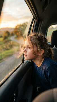 Petite fille pensive regardant par la fen&ecirc;tre d'une voiture au coucher du soleil