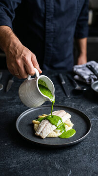 Chef cuisinier versant une sauce verte sur un filet de poisson blanc dress&eacute;