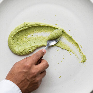 Vue de dessus d'un chef cuisinier dressant une pur&eacute;e verte sur une assiette blanche avec une cuill&egrave;re