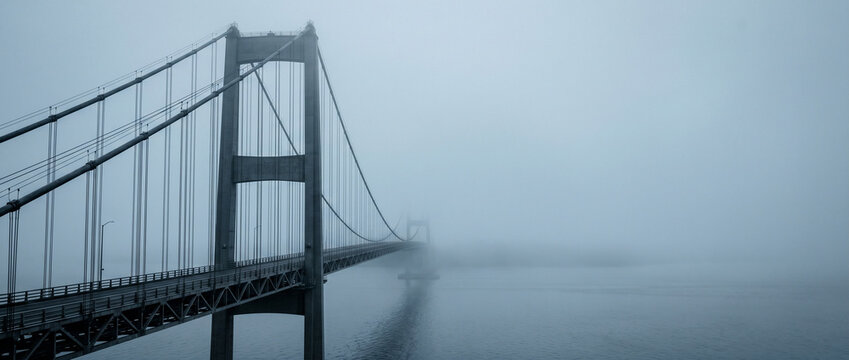 Grand pont suspendu m&eacute;tallique disparaissant dans une brume &eacute;paisse et myst&eacute;rieuse au-dessus de l'eau