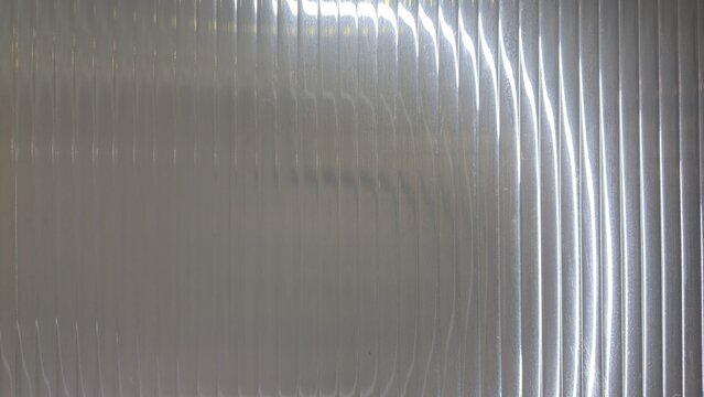 Translucent white corrugated polycarbonate sheet texture background. Close-up of ribbed polycarbonate panel with soft light reflections, perfect for modern abstract backdrops.