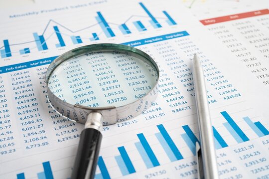 Close up view of magnifying glass over financial spreadsheet and bar charts for detailed business data inspection with analysis