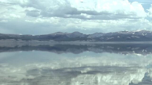 Behold Lake Khuvsgul in Mongolia, its tranquil surface a flawless mirror reflecting snow-dusted mountain ranges and a breathtaking, cloud-strewn sky. A sublime natural vista.