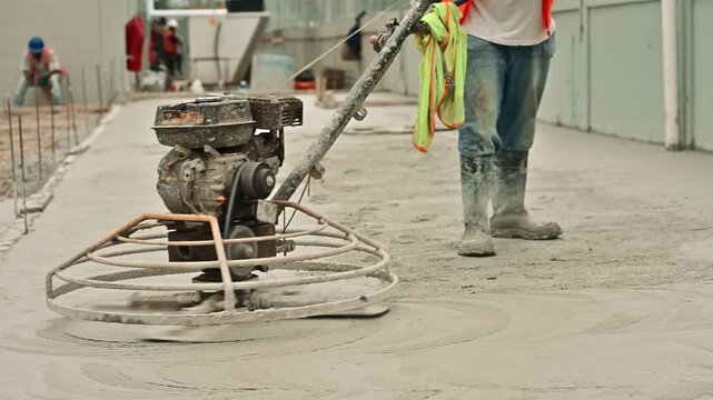 Construction worker using a power trowel machine for finishing a wet concrete floor at a building site