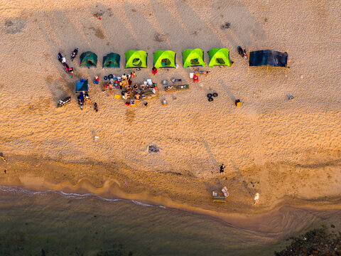 Aerial view of colorful tents set up on the sandy beach of Bai Hum with people gathering around and motorcycles parked nearby in Vinh Hai, Khanh Hoa, Vietnam.