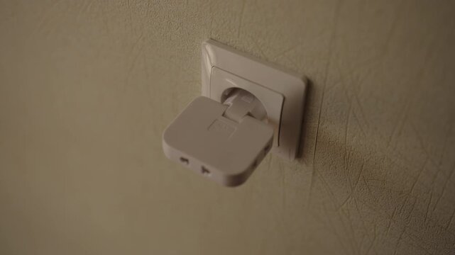 Human hand plugging white multi socket power adapter into wall outlet and connecting two different electrical cords to splitter for supplying power to multiple devices, close-up, slow motion.