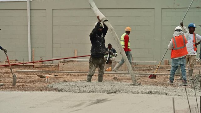 Construction workers pouring liquid cement from a pump hose to create a solid foundation slab