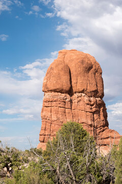 Close up of large rock formation in the desert in Moab, UT in Arches National Park near Balanced Rock. Red Rock and sagebrush, blue sky, and clouds in the desert. Arches National Park in Utah.