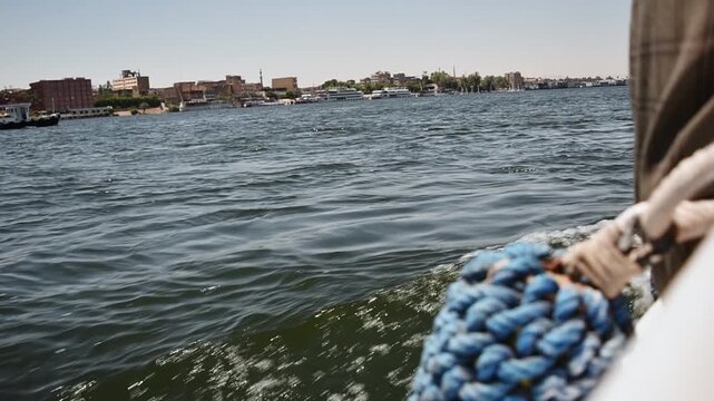 Boat ride on Nile reveals rippling water, urban shoreline and river vessels under clear sky from onboard travel viewpoint.