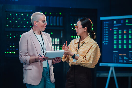 Two diverse women it specialists discussing and managing information technology operations in a secure server room environment