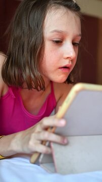 Focused girl plays touchscreen game on tablet while relaxing indoors, showing childhood leisure and digital entertainment