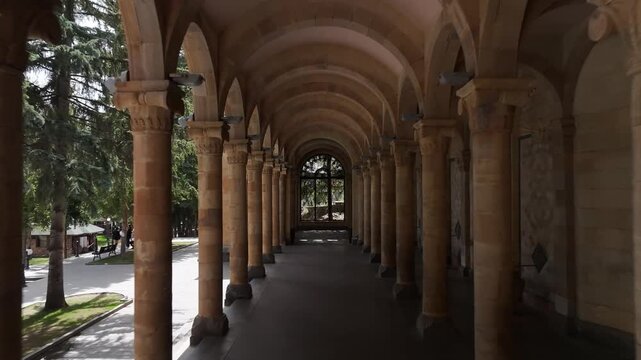 Walk through the beautiful stone colonnade of the historic Jermuk Mineral Water Gallery in Armenia, showcasing classical architecture with elegant arches and columns on a bright sunny day.


