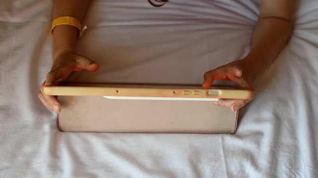 Child plays game on touchscreen tablet while relaxing on bed in hotel room during quiet indoor leisure time on vacation.