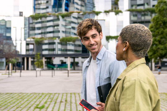 Two diverse colleagues in casual business attire discussing a project outdoors. Engaging in professional communication and teamwork