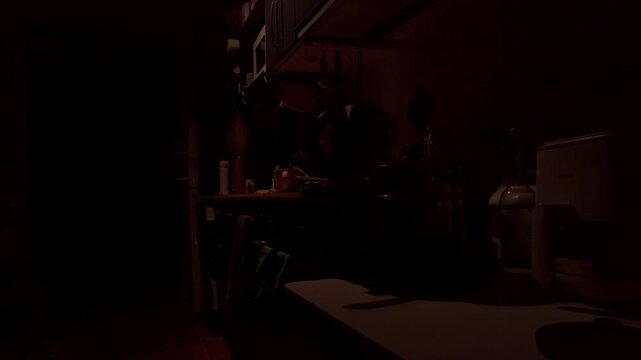 A dimly lit kitchen inside a small New Zealand studio apartment during the early morning. Soft natural light begins to enter the room while countertops, cookware