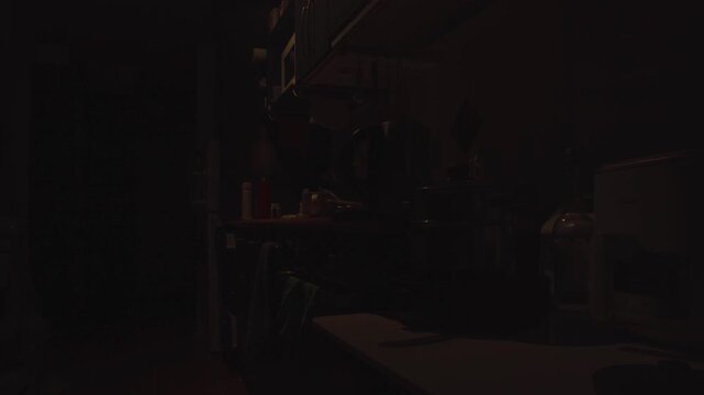 A dimly lit kitchen inside a small New Zealand studio apartment during the early morning. Soft natural light begins to enter the room while countertops, cookware