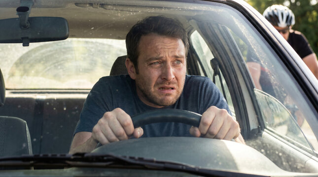 Stressed man driving car looking terrified at cyclist