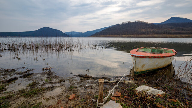 Old wooden fishing boat tied to a wooden post on a lake shore with rolling hills background