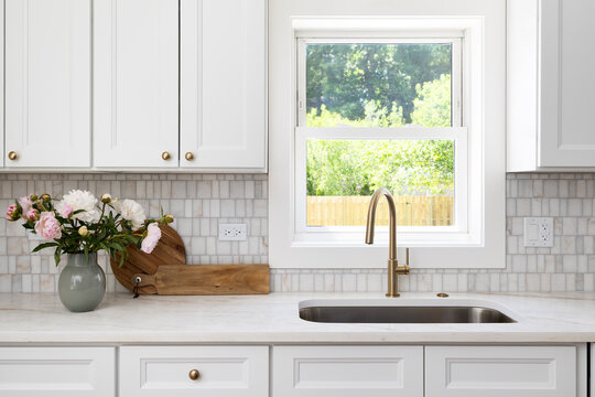 A kitchen detail with white cabinets, gold faucet, marble tiled backsplash, and a granite countertop.