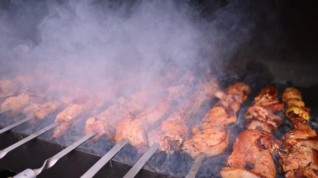 Rows of chicken skewers sizzle over hot grill. Smoke rises as meat cooks
