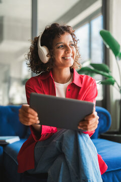 Young latin woman student using digital tablet technology for education, online browsing, studying in office or campus. Indian or muslim girl holding tablet for work looking aside dreaming. Vertical