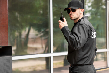Obraz premium Bodyguard with earpiece using walkie talkie near building outdoors, space for text