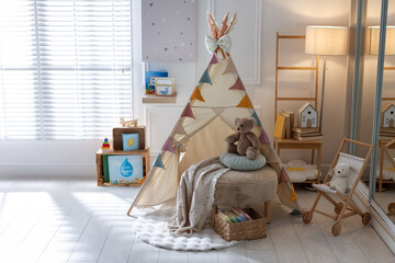 Beautiful wigwam, ottoman, different toys and books in child's room. Interior design © New Africa