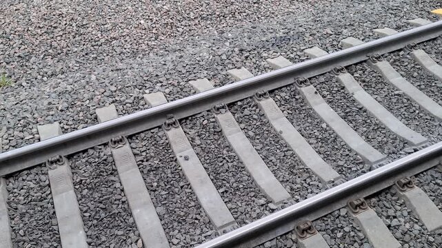 Modern railway track with concrete sleepers and grey gravel ballast. Industrial pattern of steel rails, metallic fasteners, stone crushed rock. Public transport infrastructure, train tracks