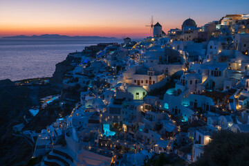 Twilight cityscape of Oia’s whitewashed buildings and blue domes overlooking the Aegean Sea, with warm lights glowing at dusk. © Andrei Tomas