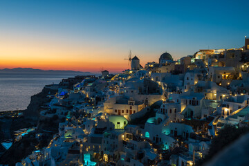Illuminated whitewashed houses and church domes in Oia, Santorini, overlooking the Aegean Sea at blue hour with colorful sunset horizon. © Andrei Tomas