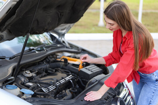 Woman checking motor oil level in car with dipstick outdoors