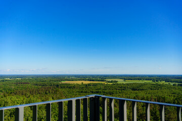 Fototapeta premium Scenic view of green forest and yellow agriculture fields from an observation tower. Panoramic aerial lookout of vast nature countryside and rural farmland under blue sky.
