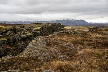 Fototapeta premium Volcanic fissure along the Mid-Atlantic Ridge with a snow-capped mountain in the background under cloudy skies in Thingvellir National Park Iceland