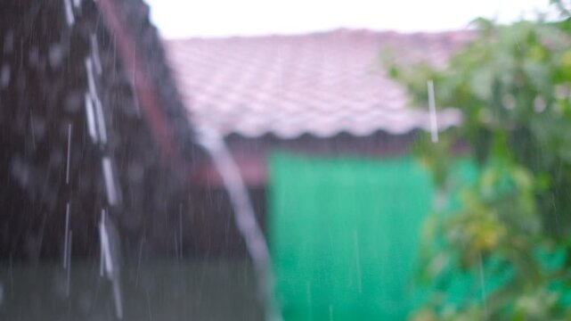 Rain streams down tiled roof, green fence visible