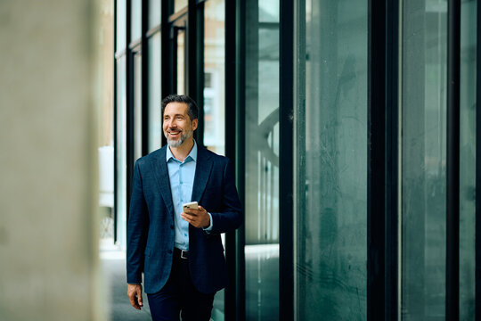 Happy businessman with cell phone walking in the city.