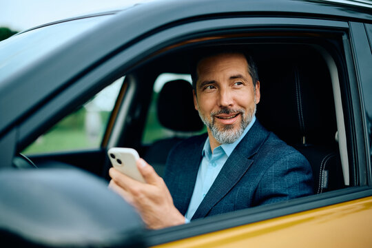 Male executive using smart phone while driving a car.