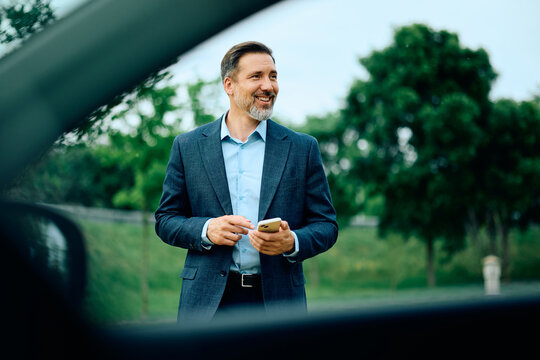 Happy businessman checking his smart phone before getting into a car.