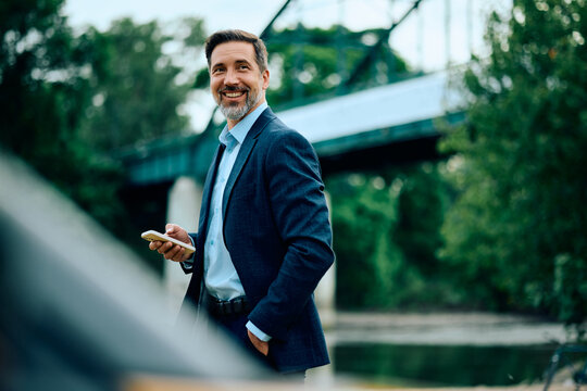 Happy entrepreneur with mobile phone in nature looking away.