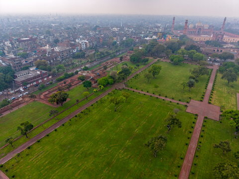 Aerial view of Lahore Fort featuring expansive green lawns, manicured pathways, and historic Badshahi Mosque in the background, set against the urban cityscape of Lahore, Punjab, Pakistan.